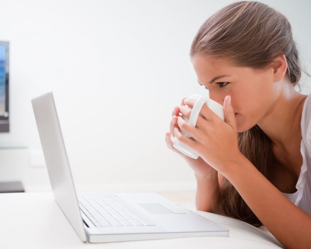 Young woman taking a sip of coffee while surfing the internet in the living room