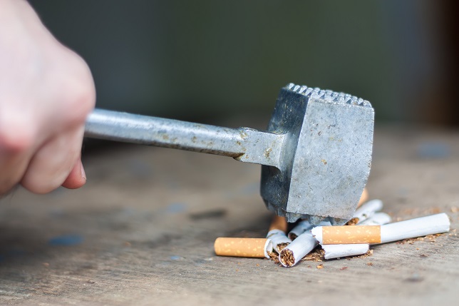 Quit smoking, human hand breaking cigarettes with hammer